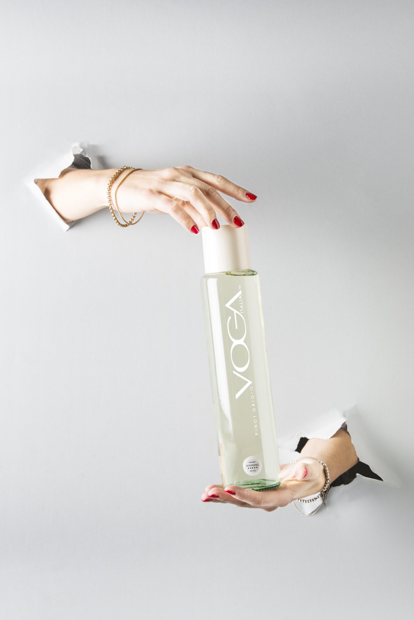 A hand offering a bottle of VOGA Pinot Grigio through torn paper